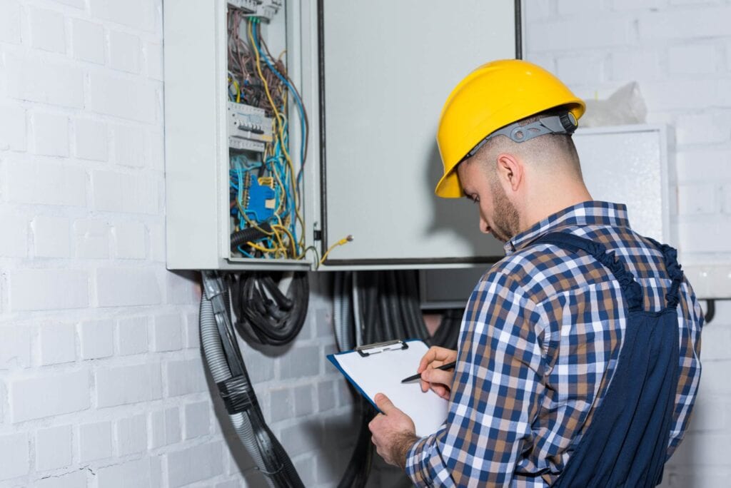Electrician or technician in a plaid shirt, blue overalls, and yellow hard hat