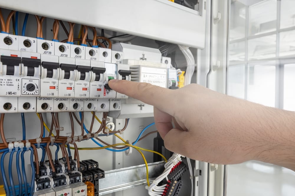 Close-up of a hand flipping a switch on a modern electrical circuit breaker panel with organized wiring.