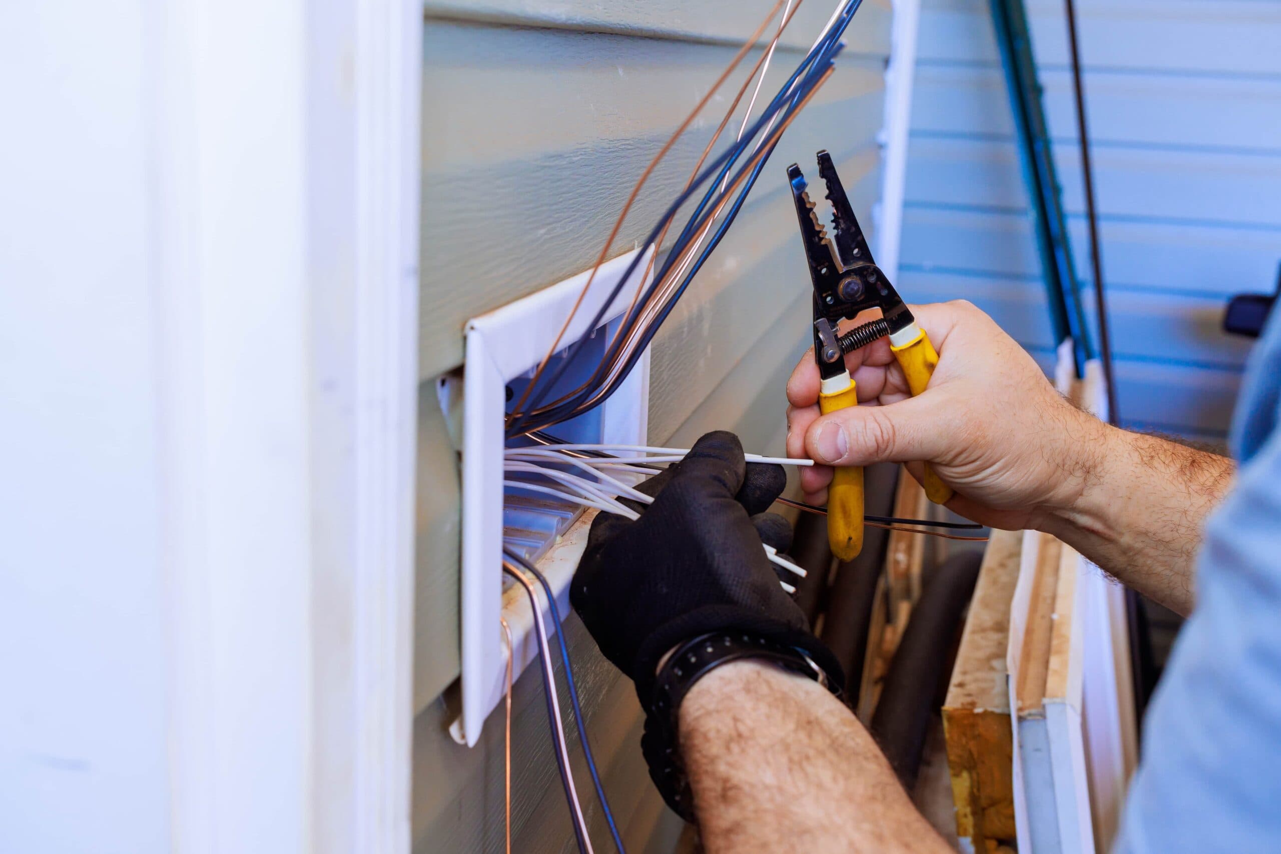 Florida Lanai Electrical Upgrades for The Ultimate Safety Guide 1 Close-up of a technician's hands in black protective gloves using yellow-handled wire strippers to prepare electrical cables at an exterior wall outlet box.