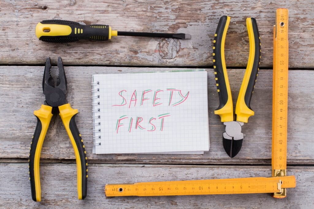 Top-down view of hand tools including pliers, a screwdriver, wire cutters, and a folding ruler arranged around a notebook with the handwritten slogan 