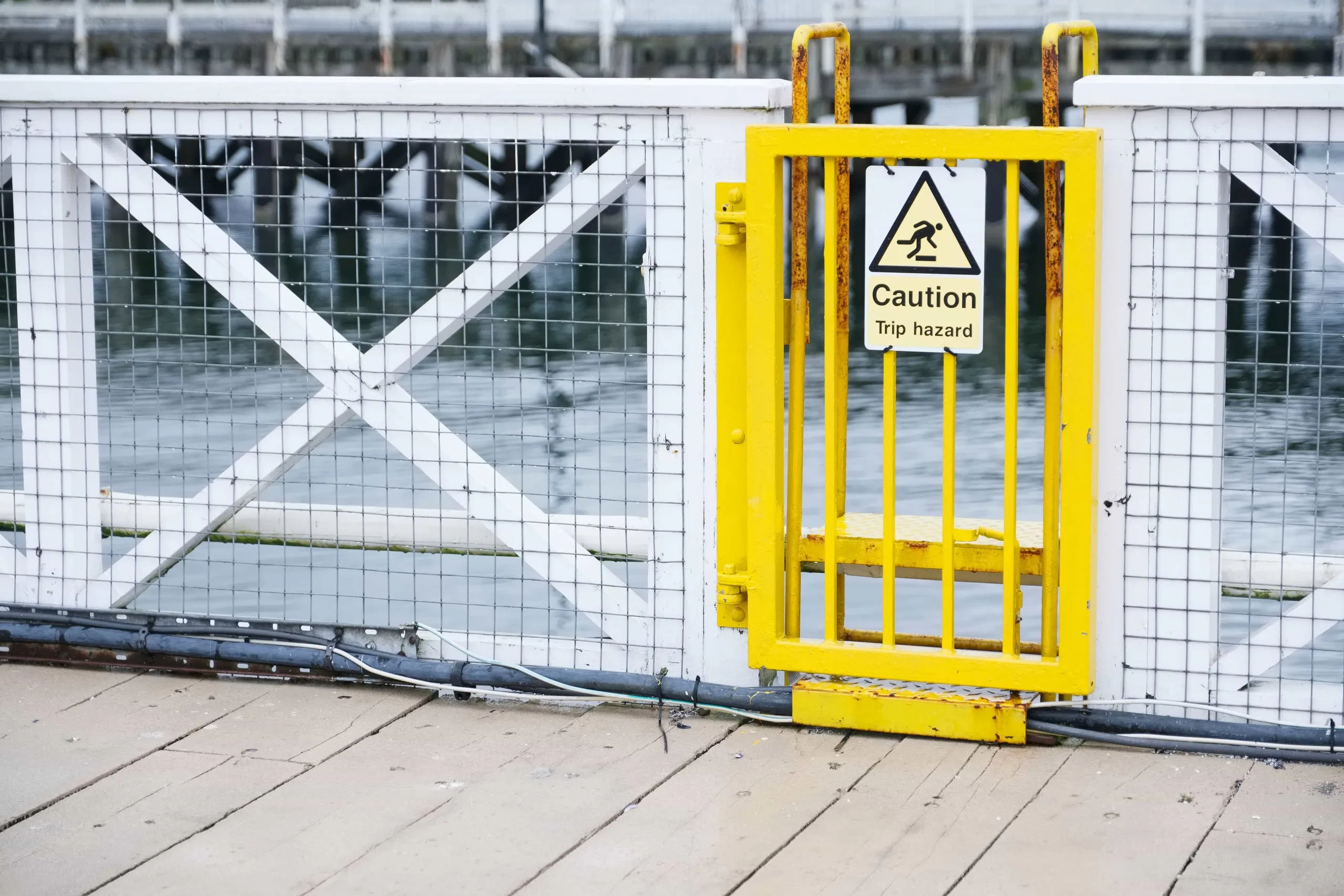 A yellow metal safety gate with a "Caution Trip Hazard" sign on a wooden dock in Tampa, Florida, emphasizing workplace safety compliance.